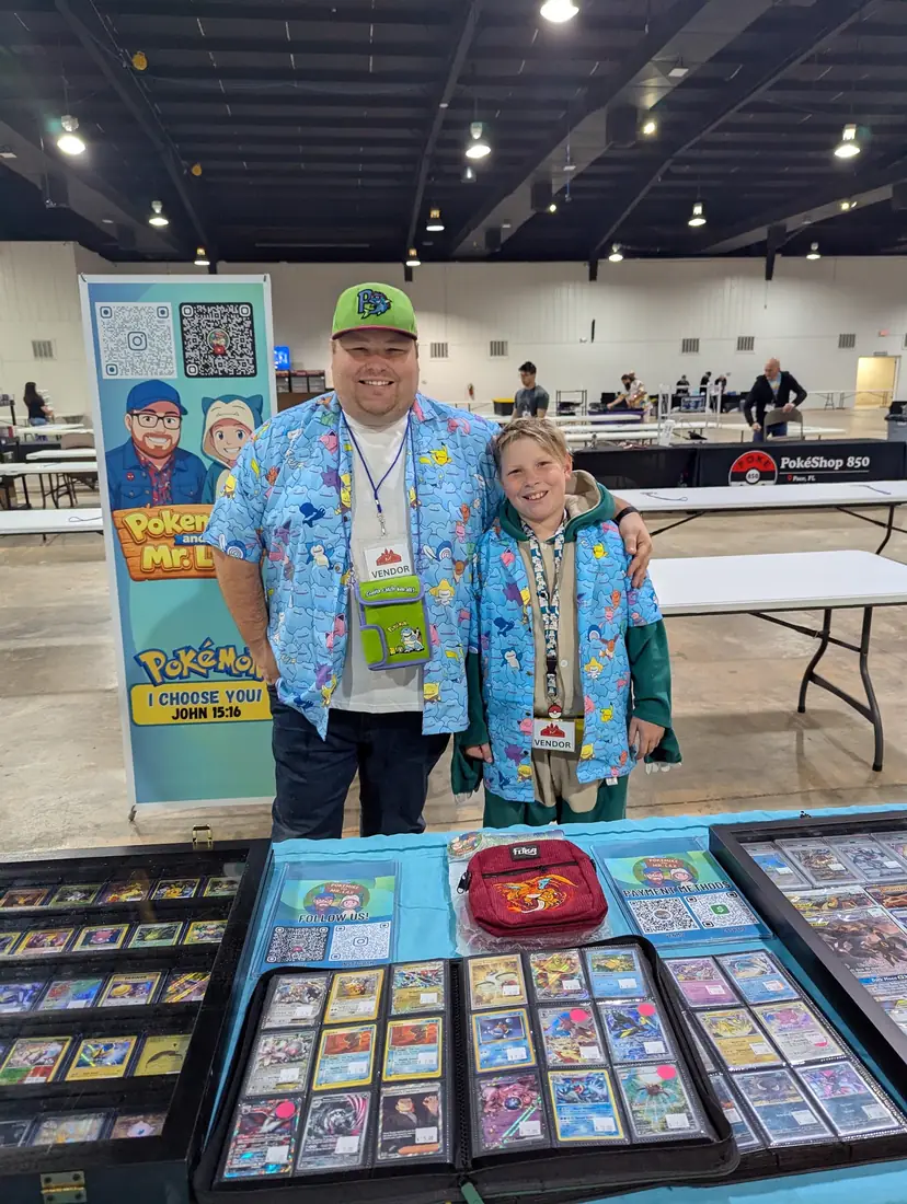 Mike and Mr. Lax behind their table of cards, with their banner standing behind them